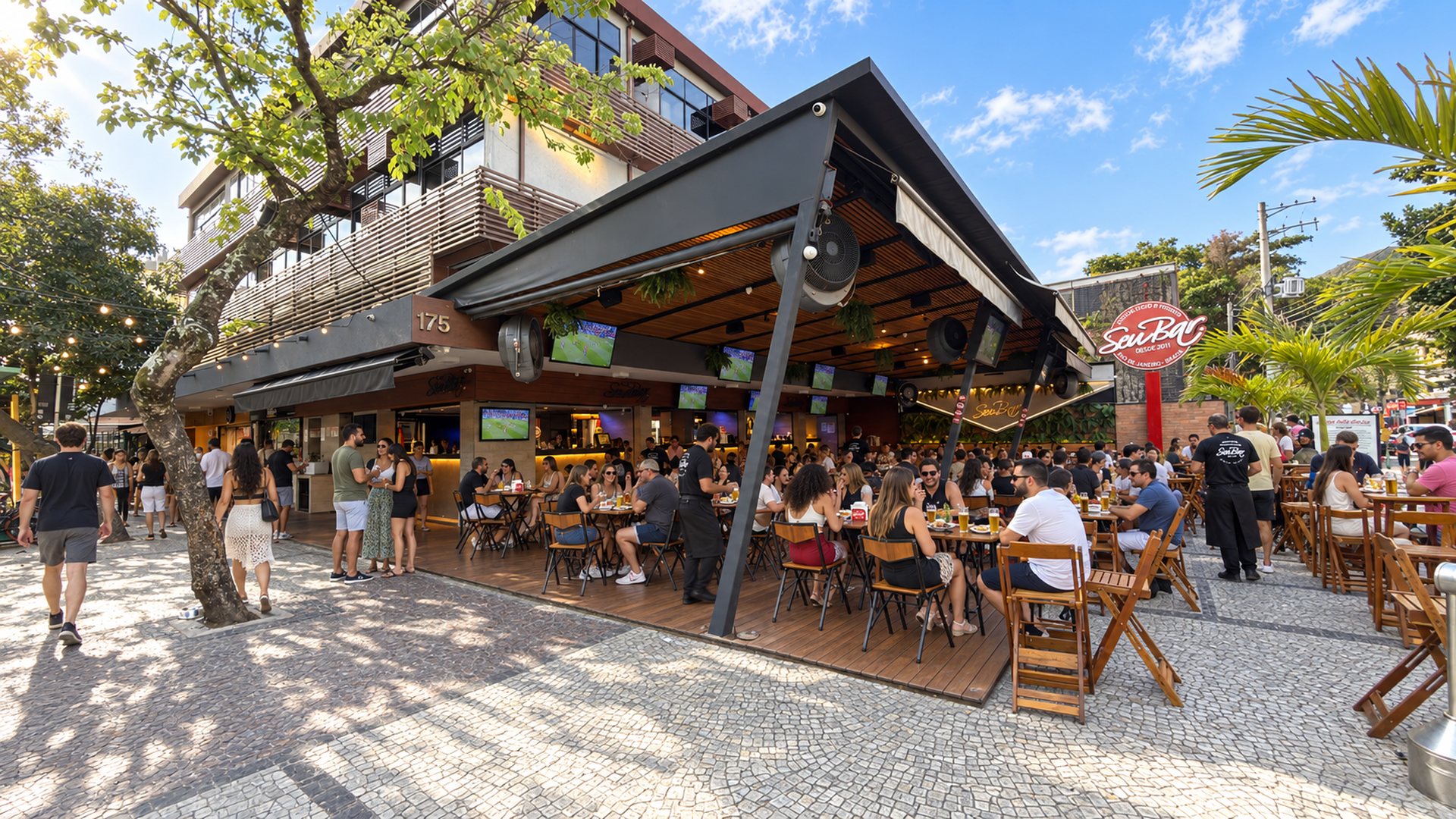 Seu Bar's facade at Av. Olegário Maciel, 175, Jardim Oceânico, Barra da Tijuca: wooden deck on the sidewalk with full tables in the late afternoon